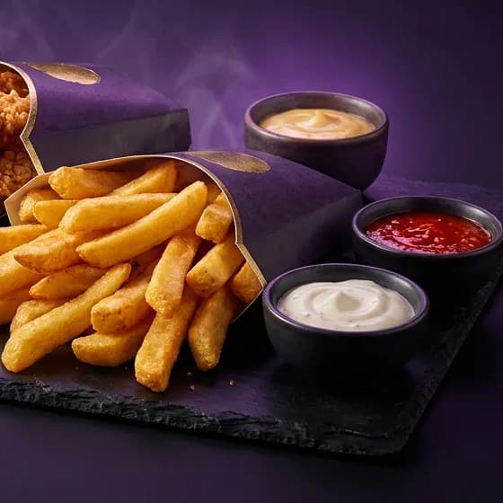 Thick-cut golden fries in a purple holder beside signature sauce pots