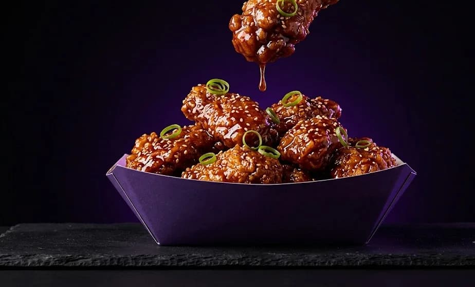 Korean-glazed crispy chicken in a purple boat with sesame and spring onion