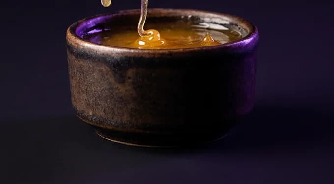 A crispy golden tender dripping with sauce above a dark ceramic pot